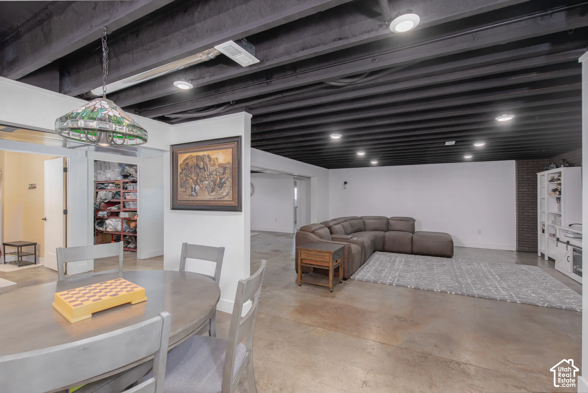 Exposed black ceiling joists with recessed lighting, stained concrete flooring, white walls, and a built-in storage system