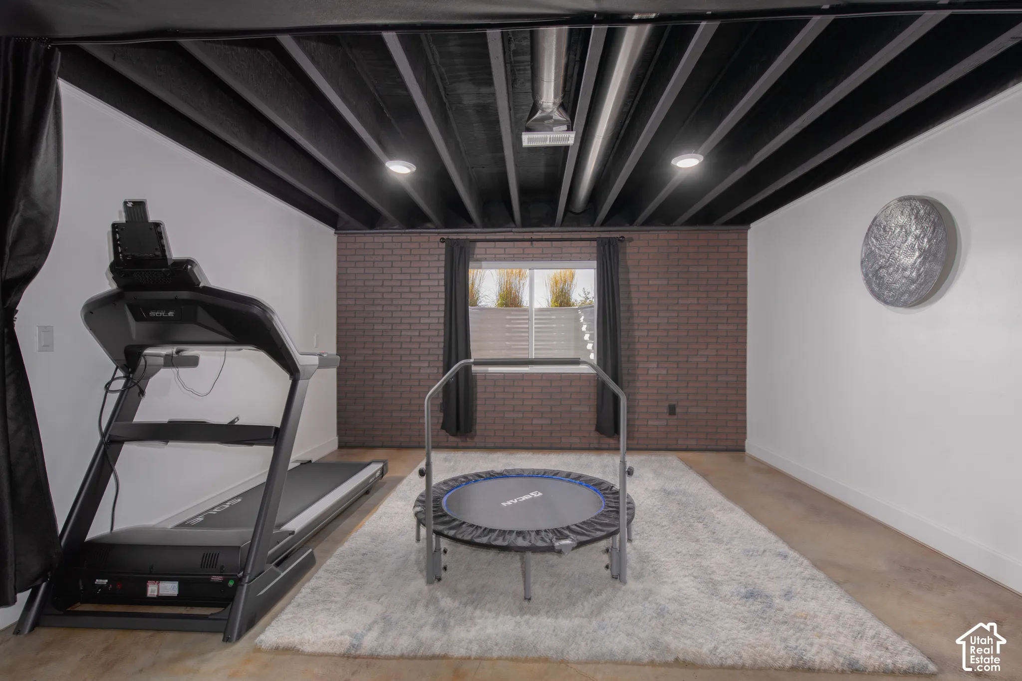 Exposed black ceiling beams with recessed lighting, brick accent wall, white painted walls, and wood-finish flooring