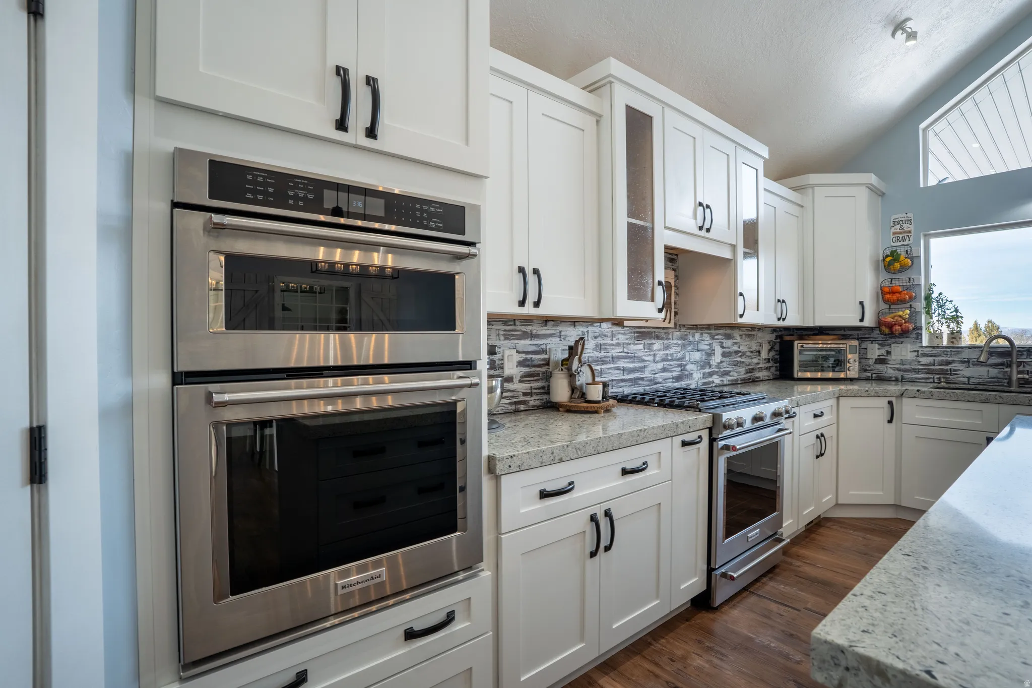 Kitchen with stainless steel appliances, white cabinetry, decorative backsplash, light stone countertops