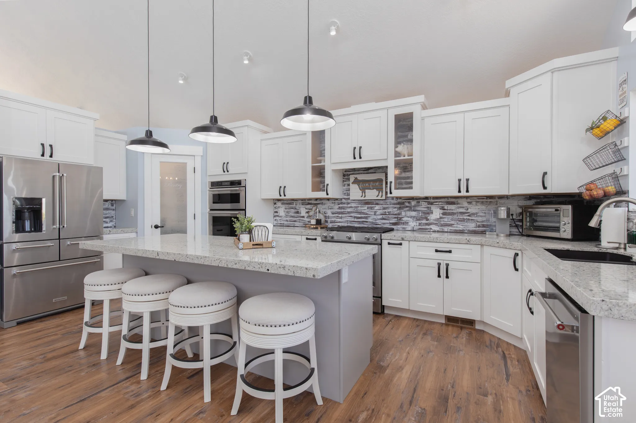 Modern kitchen featuring white cabinetry, stainless steel appliances, a large center island with counter seating, wood-finish flooring, and pendant lighting
