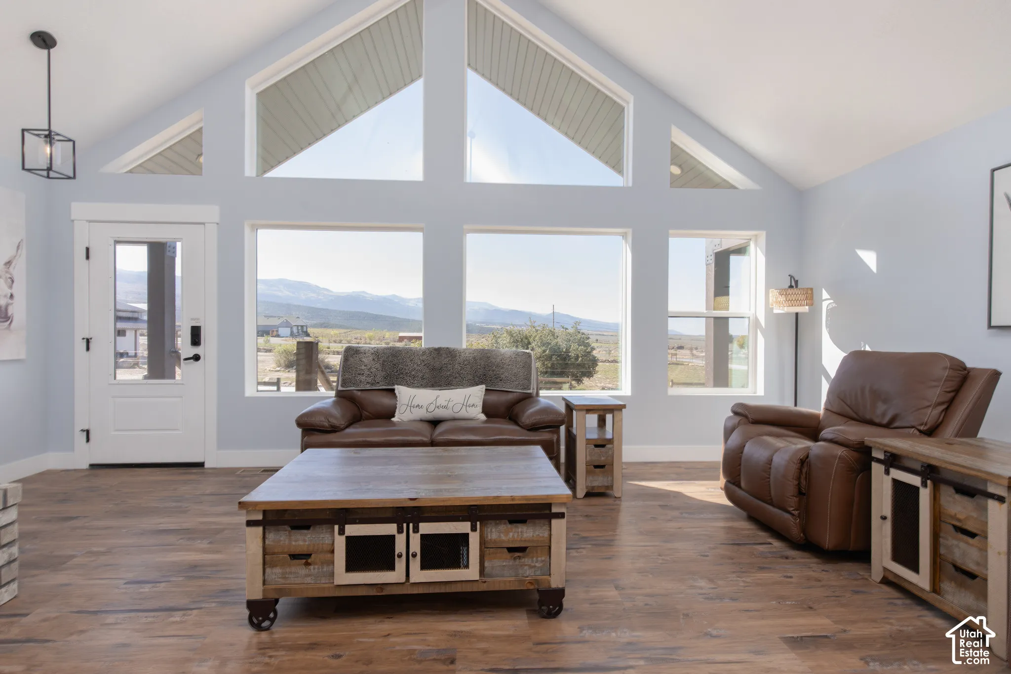 Vaulted ceiling with transom windows, wood-finish flooring, white paneled door with glass insert, and mountain scenery
