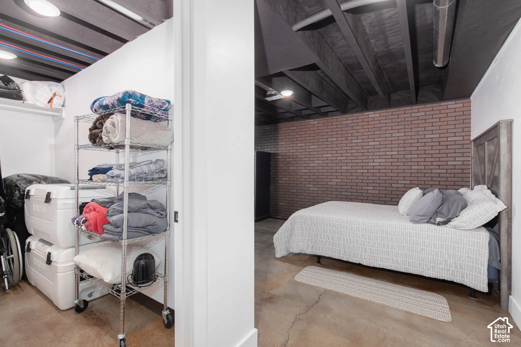 Exposed ceiling joists with painted finish, brick-patterned accent wall, and concrete flooring