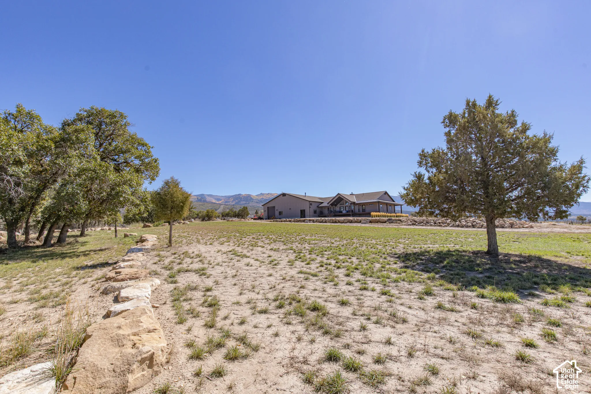 Expansive exterior space featuring a natural stone border, mature trees, and distant mountain scenery