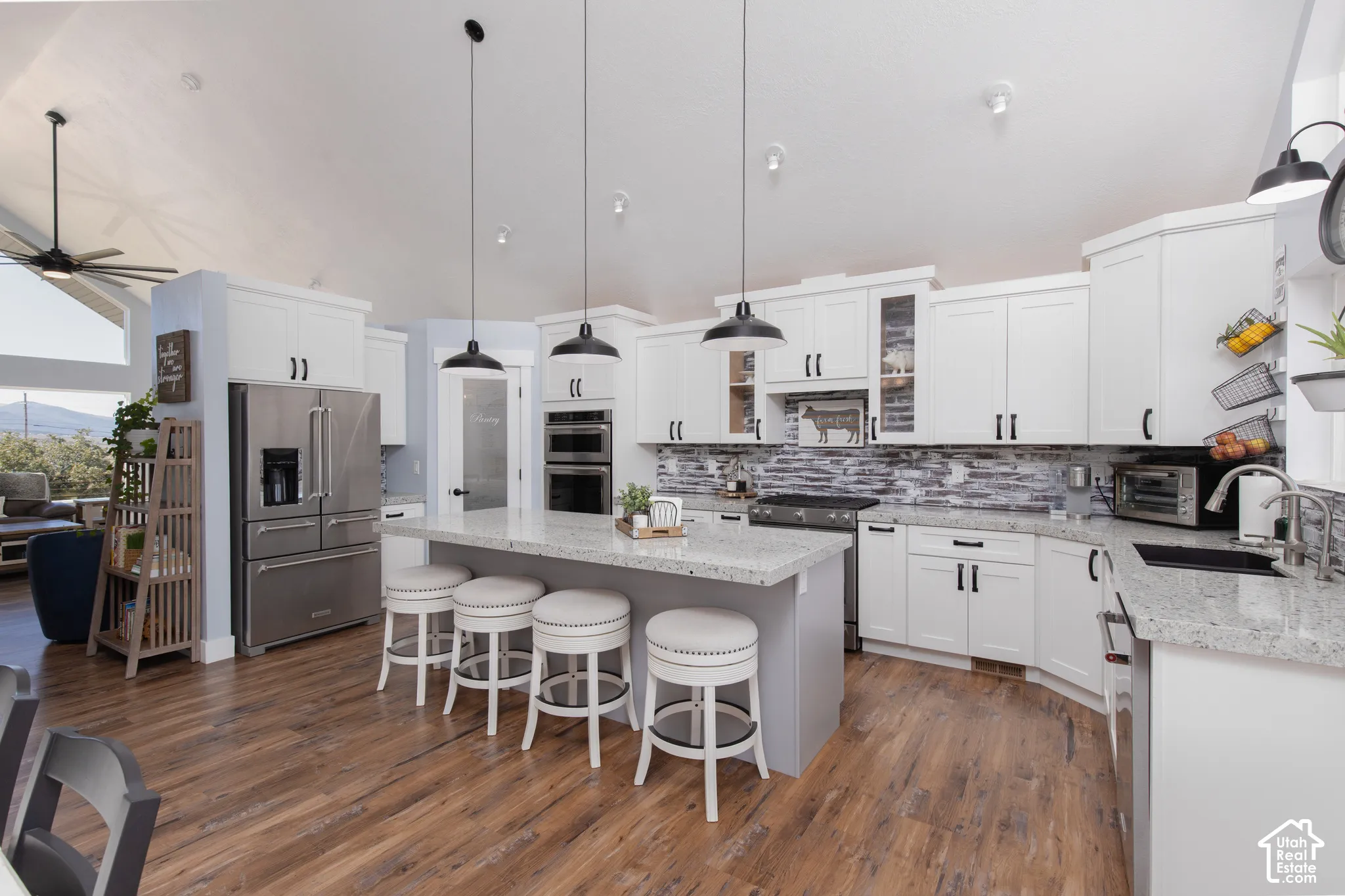 Vaulted ceiling, wood-finish flooring, white cabinetry with dark hardware, stainless steel appliances, and a kitchen island with stone-finish countertop