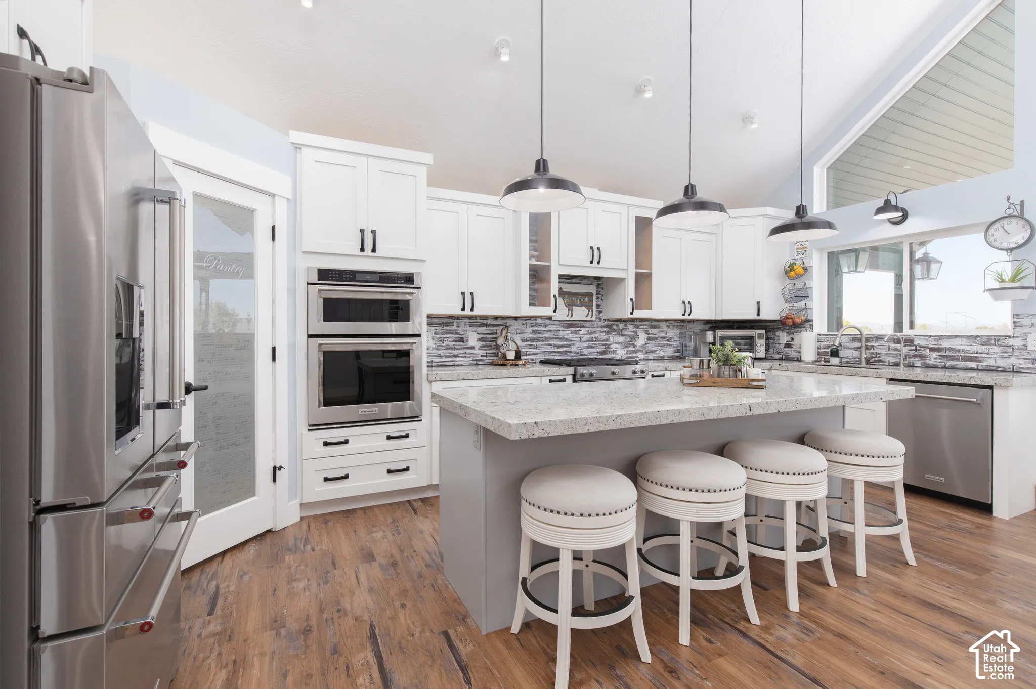 White shaker cabinetry, stainless steel appliances, wood-finish flooring, stone countertops, and a stone-tile backsplash