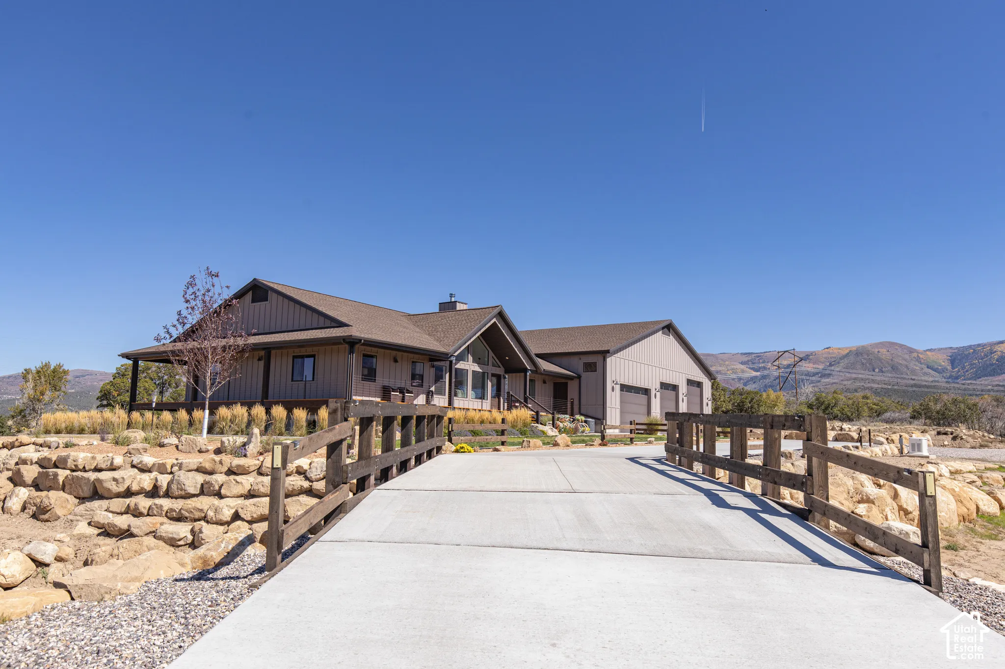 Exterior featuring a covered front porch, attached multi-car garage, concrete driveway, and natural rock landscaping