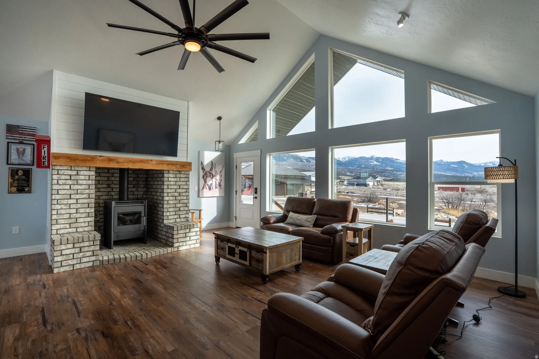 Living area featuring wood finished floors, a high ceiling, ceiling fan, and propane fireplace, large windows looking to the valley and mountains