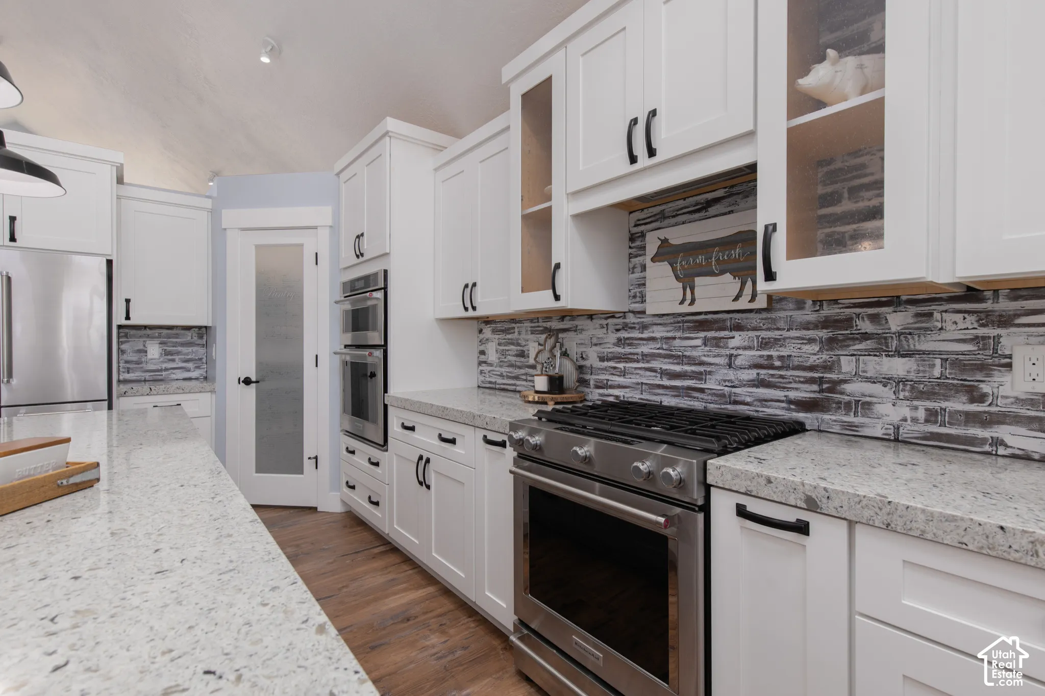 White shaker cabinetry with black hardware, stainless steel appliances, patterned backsplash, light-toned countertops, and wood-finish flooring