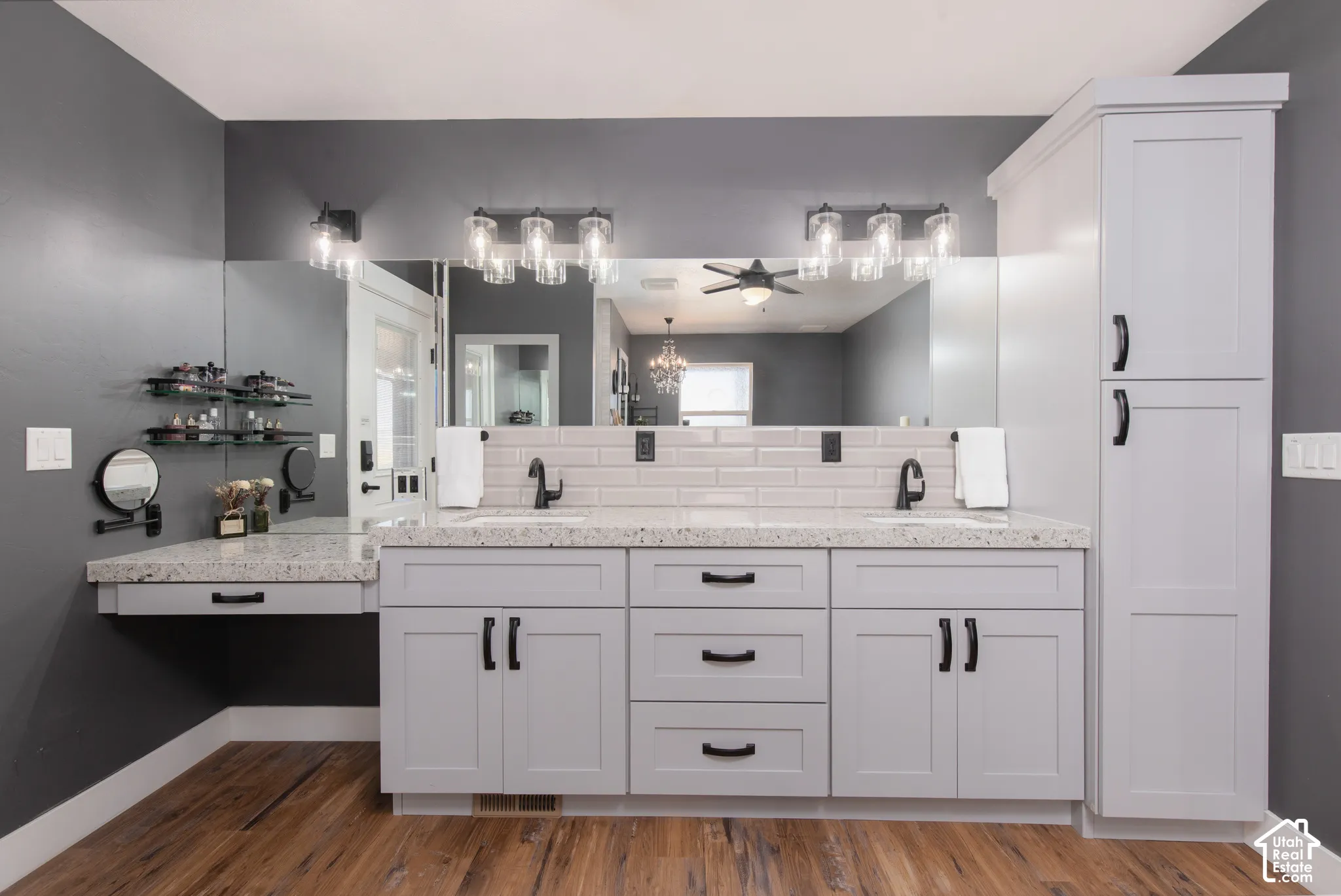 Double vanity with light gray cabinetry, built-in storage tower, wood-finish flooring, and subway tile backsplash