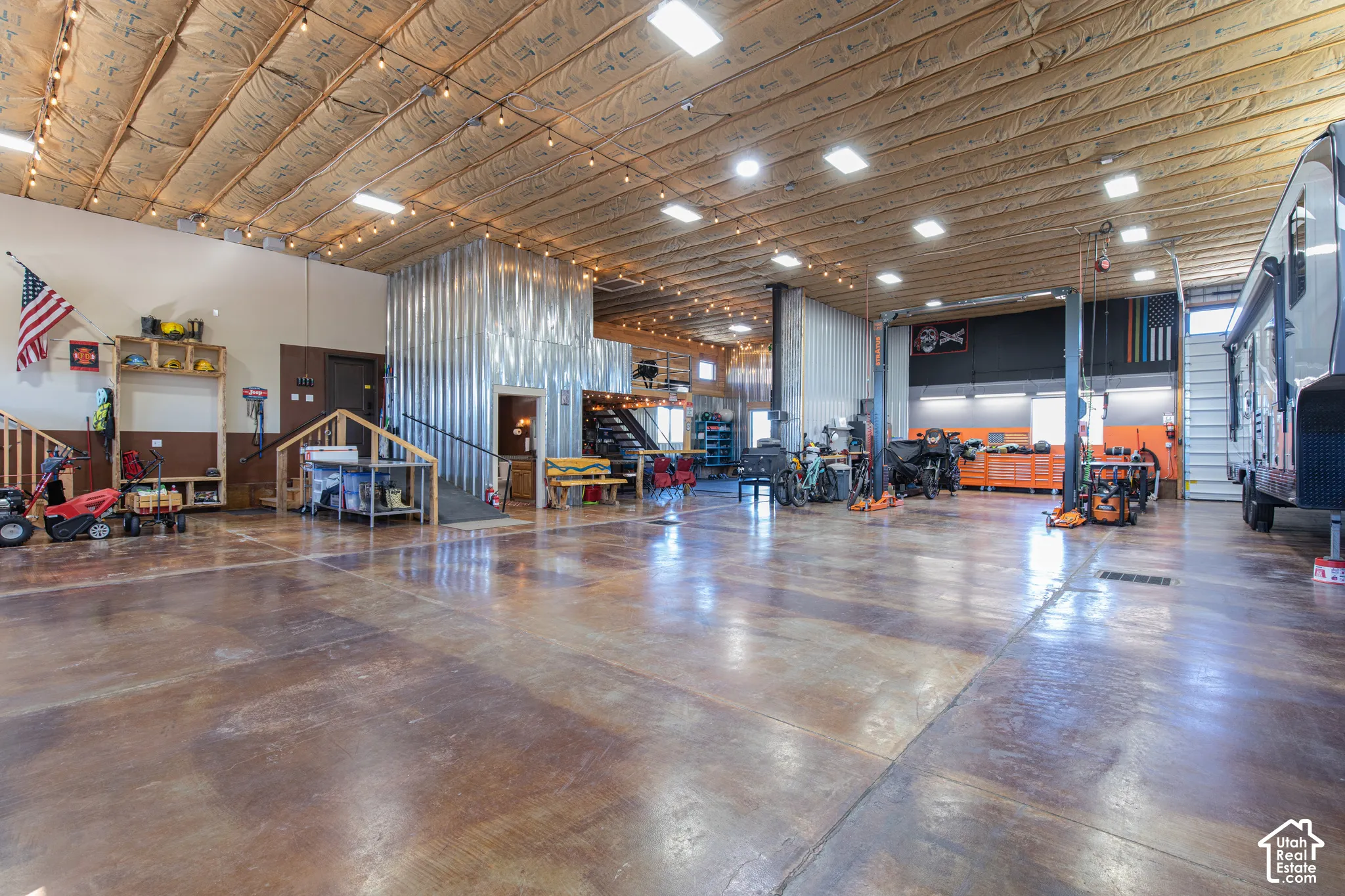 Spacious garage featuring a concrete floor, corrugated metal wall accents, and an exposed wood beam ceiling with string lighting