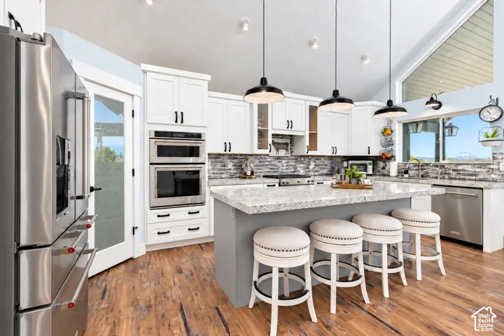 Kitchen featuring stainless steel appliances, white cabinetry, a large kitchen island with seating, wood-finish flooring, and a vaulted ceiling