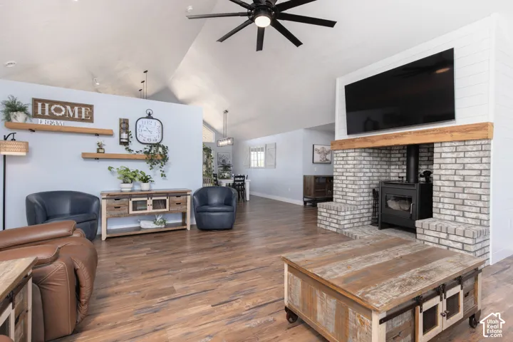 Vaulted ceiling, wood-finish flooring, brick-faced wood-burning stove, exposed wood mantel, and black ceiling fan