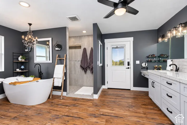 Freestanding soaking tub, wood-finish flooring, dual vanity with undermount sinks, walk-in shower with tile surround, and an exterior door