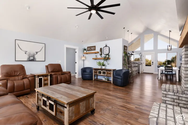 Vaulted white ceilings, wood-finish flooring, brick fireplace surround, and a ceiling fan with integrated lighting