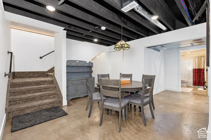 Concrete flooring with painted ceiling beams, recessed lighting, and a carpeted staircase with a dark handrail