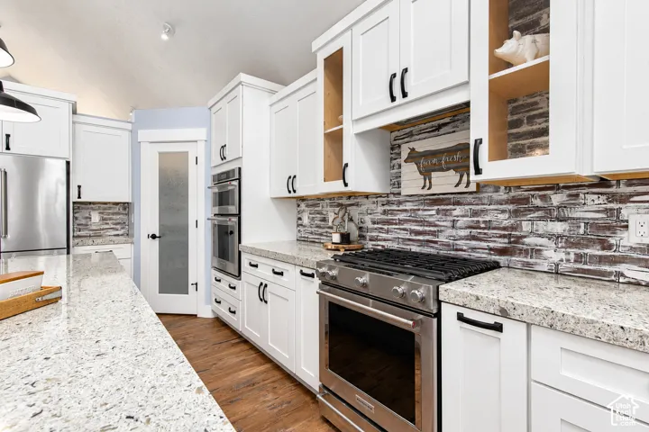 White shaker-style cabinetry, stainless steel appliances, wood-finish flooring, and a brick-patterned backsplash