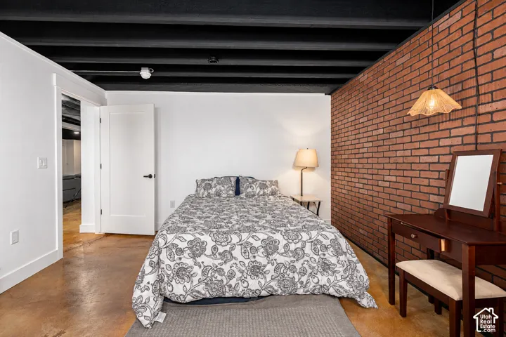Exposed brick wall accent, concrete-finish flooring, and a black open-joist ceiling