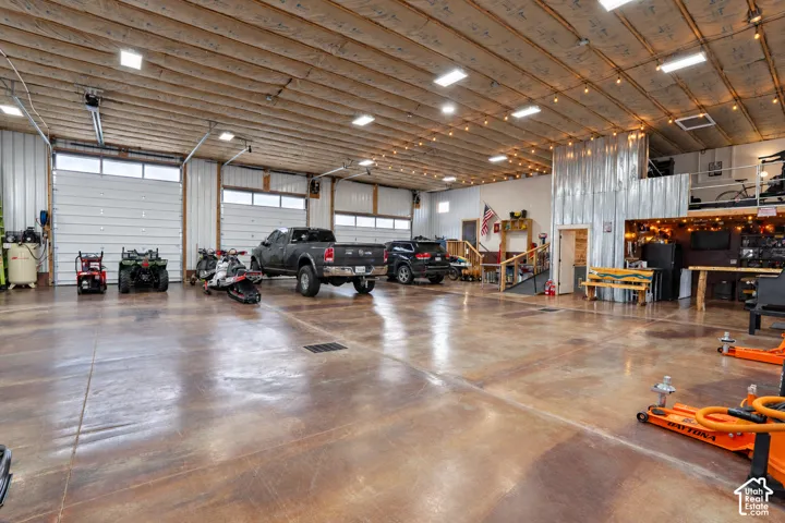 Expansive garage featuring multiple roll-up doors, polished concrete flooring, exposed wood beam ceiling, and a large metal-clad partition
