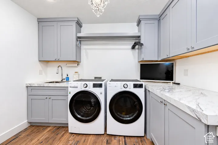 Built-in cabinetry with light gray finish, stone-finish countertops, undermount sink with chrome faucet, wood-finish flooring, and a decorative chandelier
