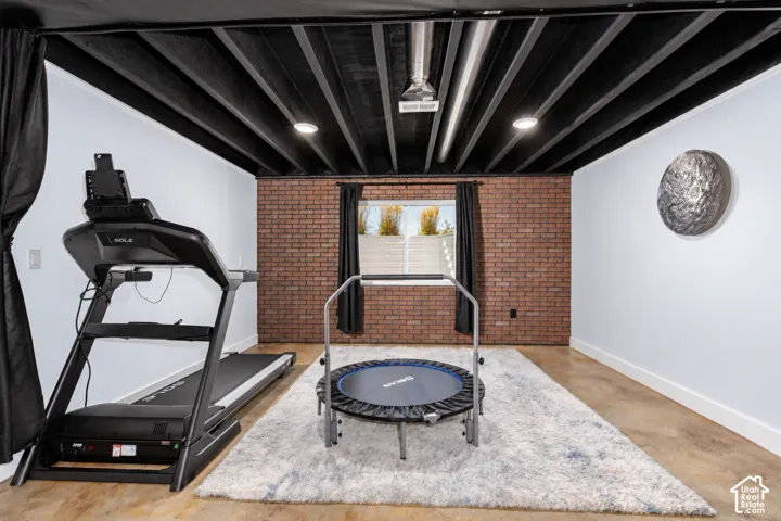Exposed black ceiling beams with recessed lighting, brick accent wall, white painted walls, and wood-finish flooring