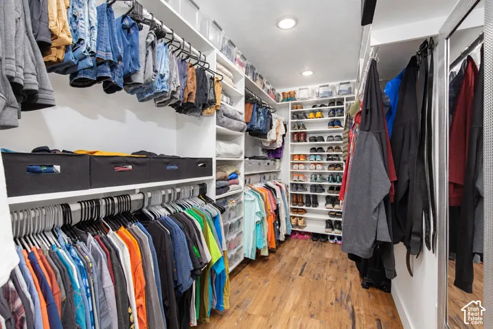 Spacious walk-in closet featuring extensive built-in shelving, multiple hanging rods, recessed lighting, and wood-finish flooring