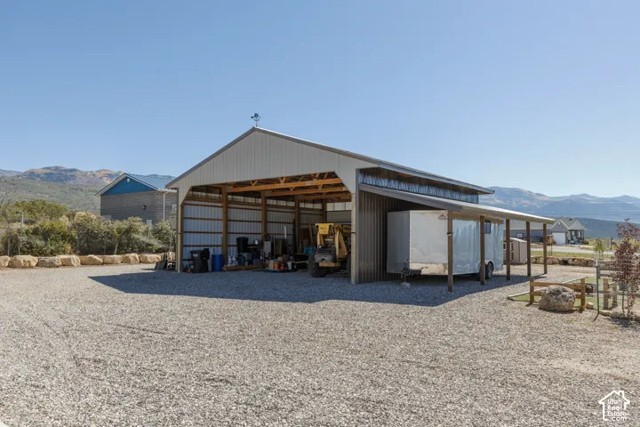 Metal-clad barn structure featuring a gable roof with a weathervane, an open-sided storage area, and a covered lean-to extension, all set on a gravel surface