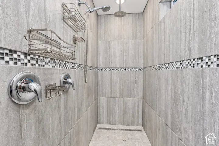 Spa-inspired shower enclosure featuring vertical wood-finish tile walls, mosaic accent band detailing, dual showerheads with chrome fixtures, and built-in shelving for convenient storage