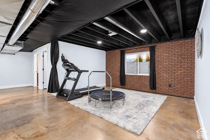 Exposed ceiling joists with painted black finish, polished concrete flooring, brick-accent wall, white interior doors, and recessed ceiling lighting