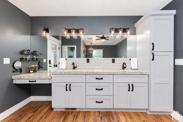 Dual vanity with light gray shaker cabinetry, integrated makeup counter, black fixtures, and wood-finish flooring