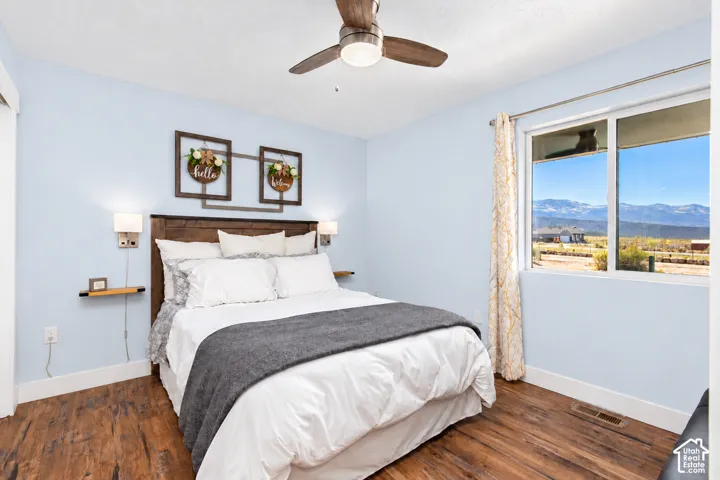 Wood-finish flooring, wood headboard, dual wall-mounted sconces, ceiling fan with integrated lighting, and a large window