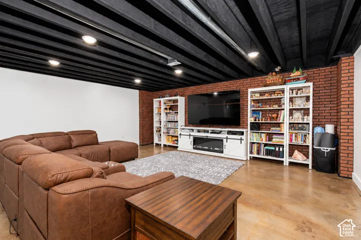 Exposed ceiling joists with a dark finish, recessed lighting, brick-finish accent wall, built-in shelving, and polished concrete flooring