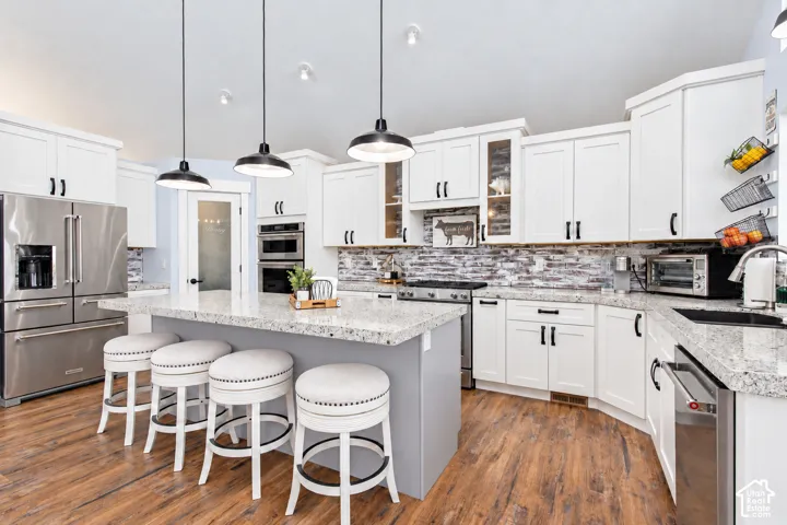 White cabinetry with black hardware, stone-finish countertops, stainless steel appliances, brick-patterned backsplash, and wood-finish flooring