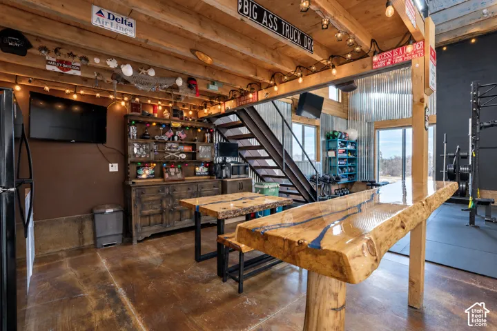 Exposed wood ceiling beams, polished concrete flooring, industrial-style staircase with metal railings, live-edge wood countertop, and corrugated metal wall accents