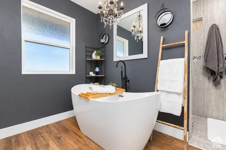 Freestanding soaking tub with a floor-mounted matte black faucet, wood-finish flooring, and a window with privacy glass
