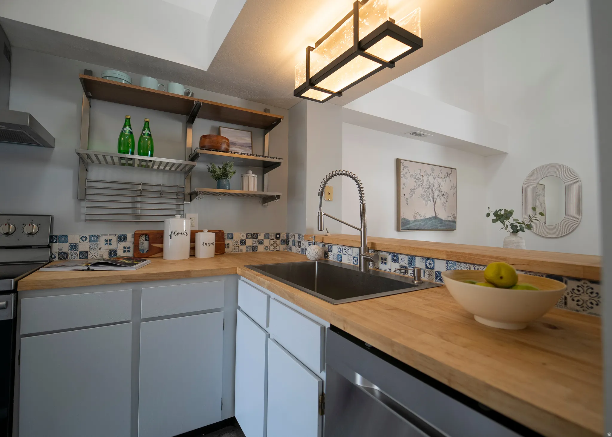 Kitchen featuring electric range oven, white cabinetry, stainless steel dishwasher, and wooden counters
