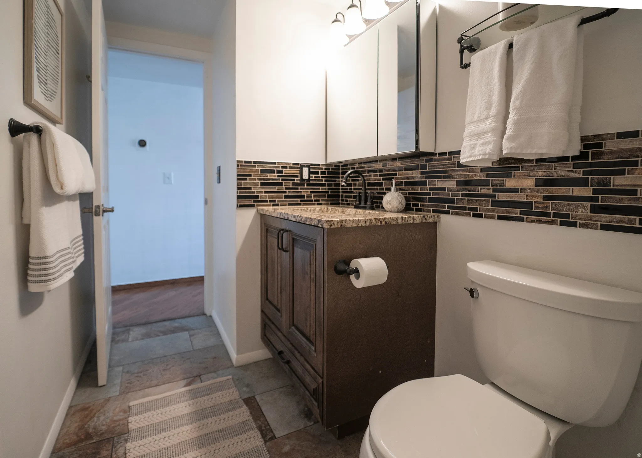Bathroom with vanity, decorative backsplash, and dark stone finish floors