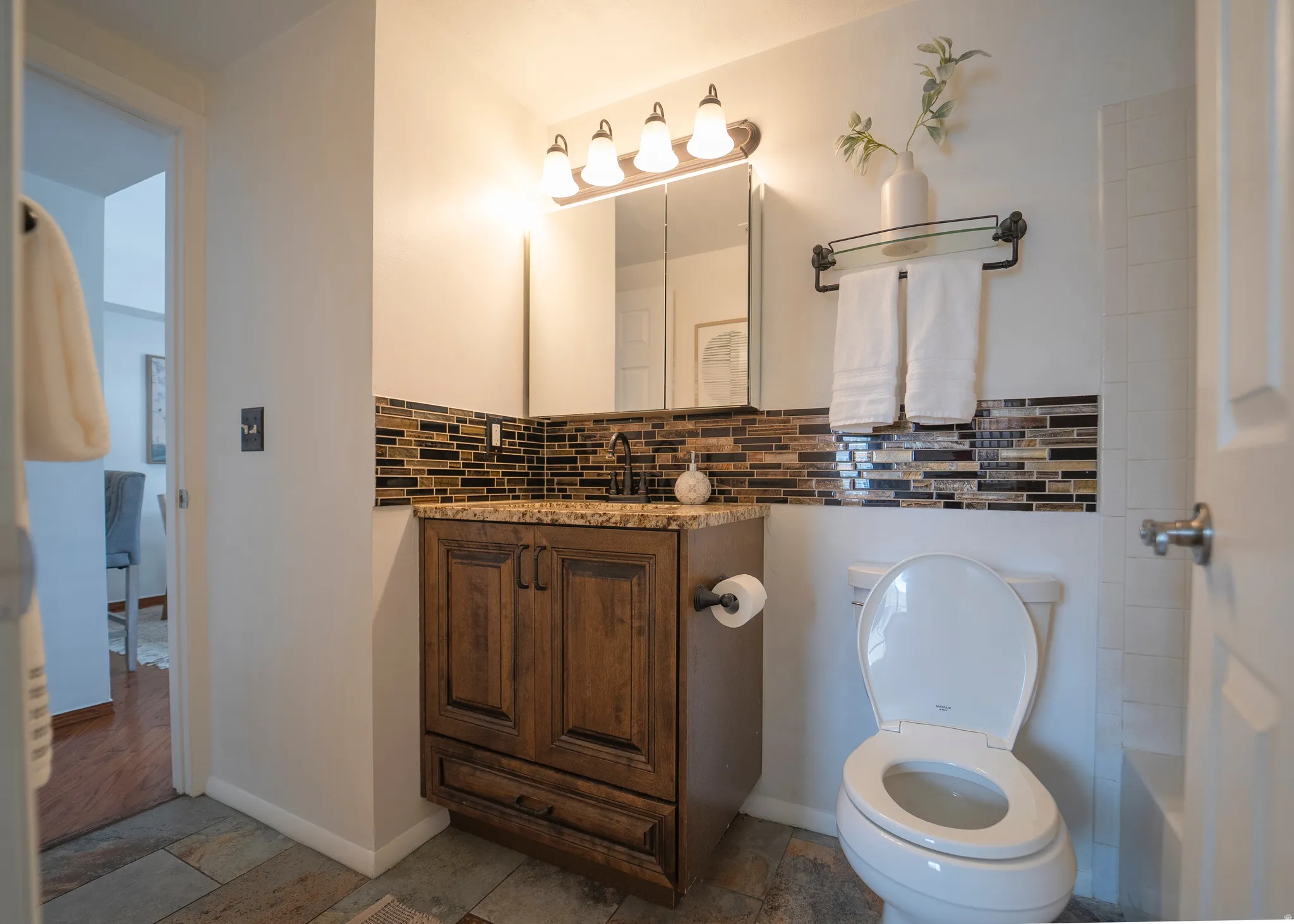 Full bath featuring vanity, decorative backsplash, and light stone finish flooring