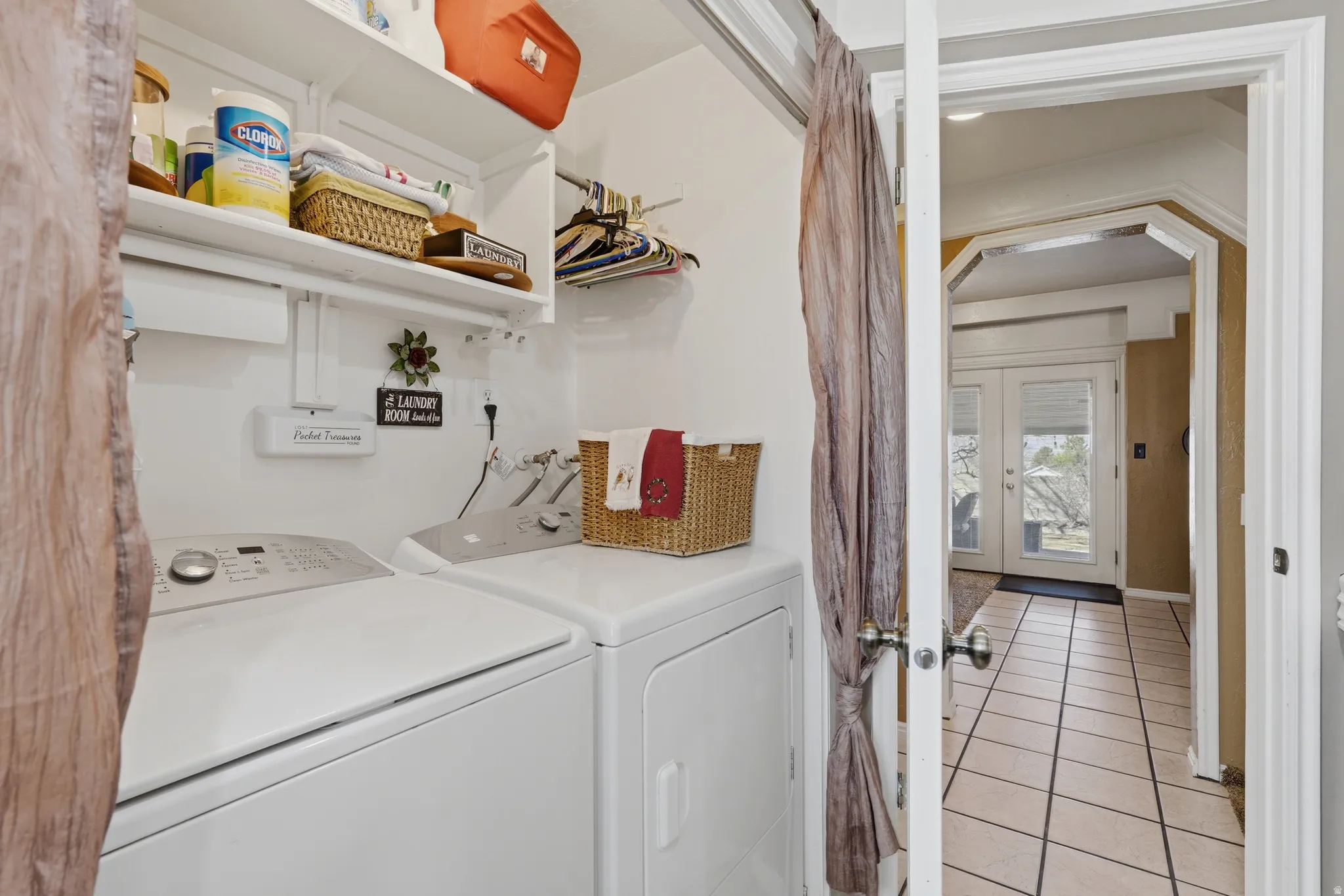 Laundry area with french doors, arched walkways, washer and clothes dryer, and light tile patterned flooring