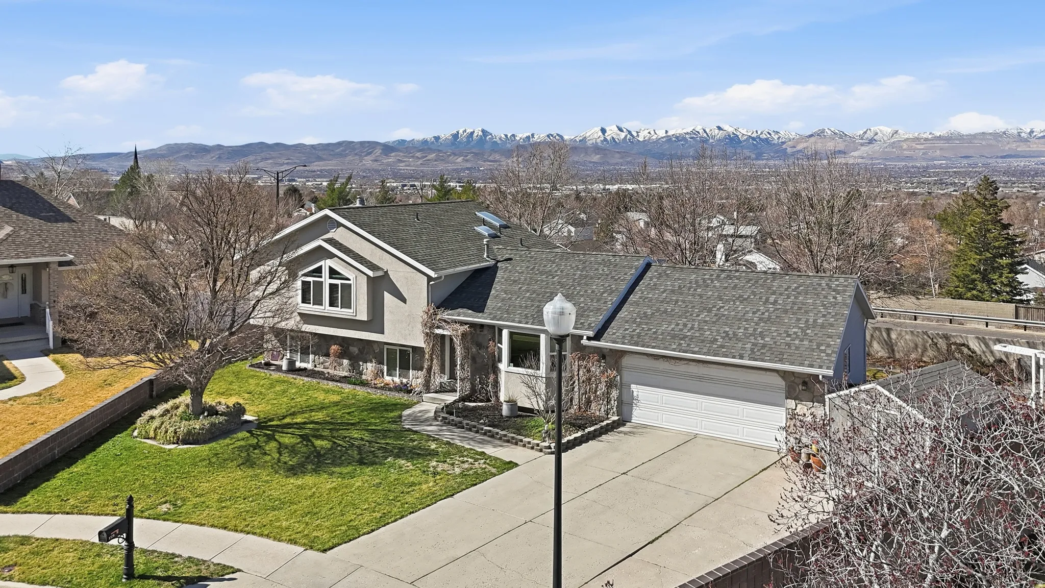 View of front of house featuring a garage, driveway, stucco siding, stone siding, and a mountain view