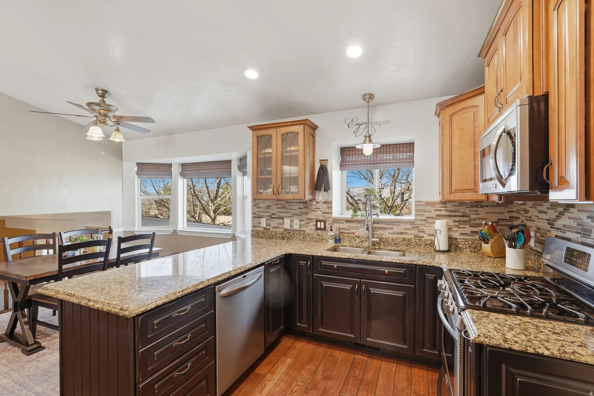 Dual tone kitchen featuring stainless steel appliances, a peninsula, light wood-type flooring, light stone counters, and two tone cabinetry