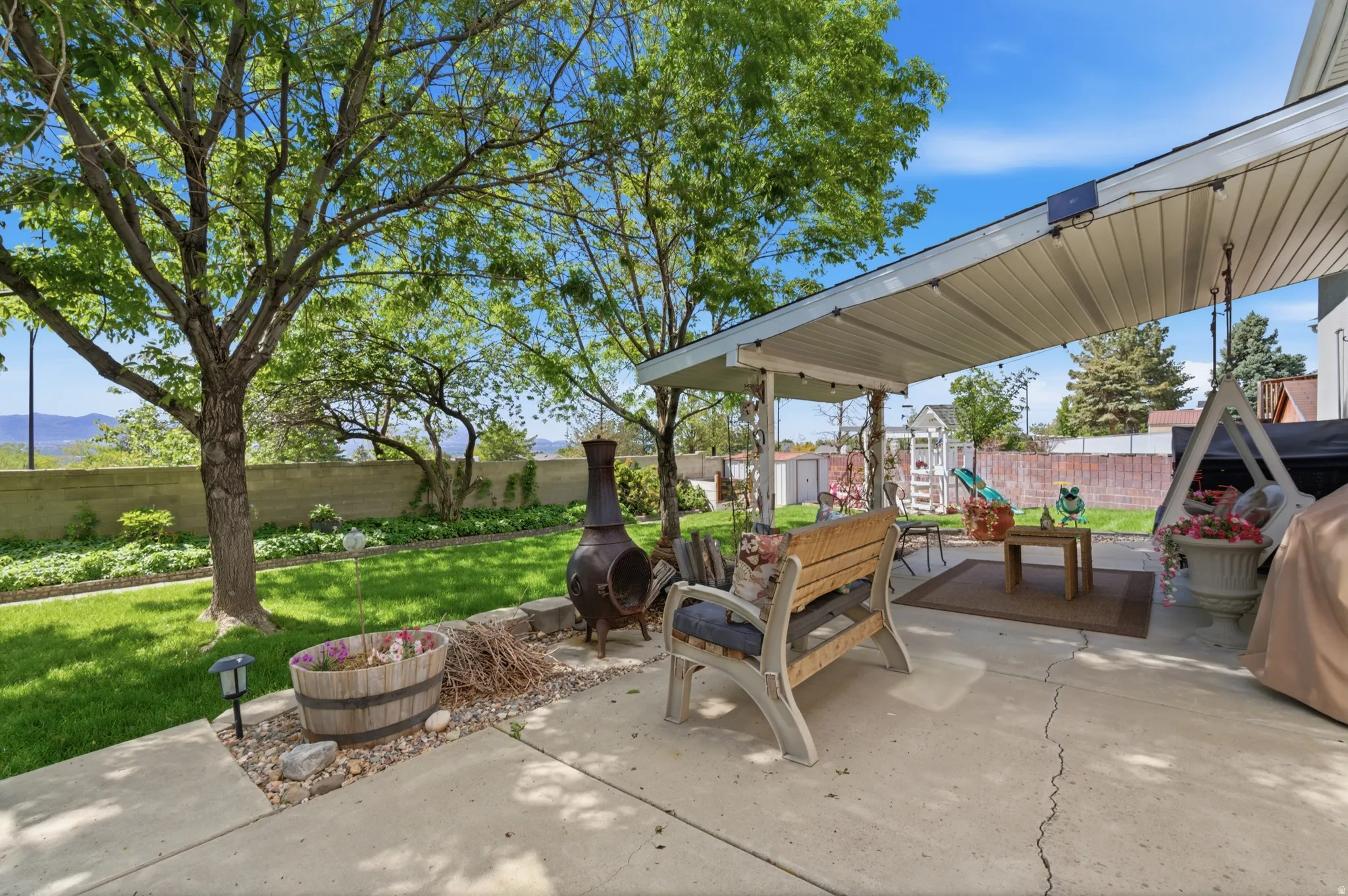 Expansive concrete patio featuring a covered awning, string lighting, and a fire pit