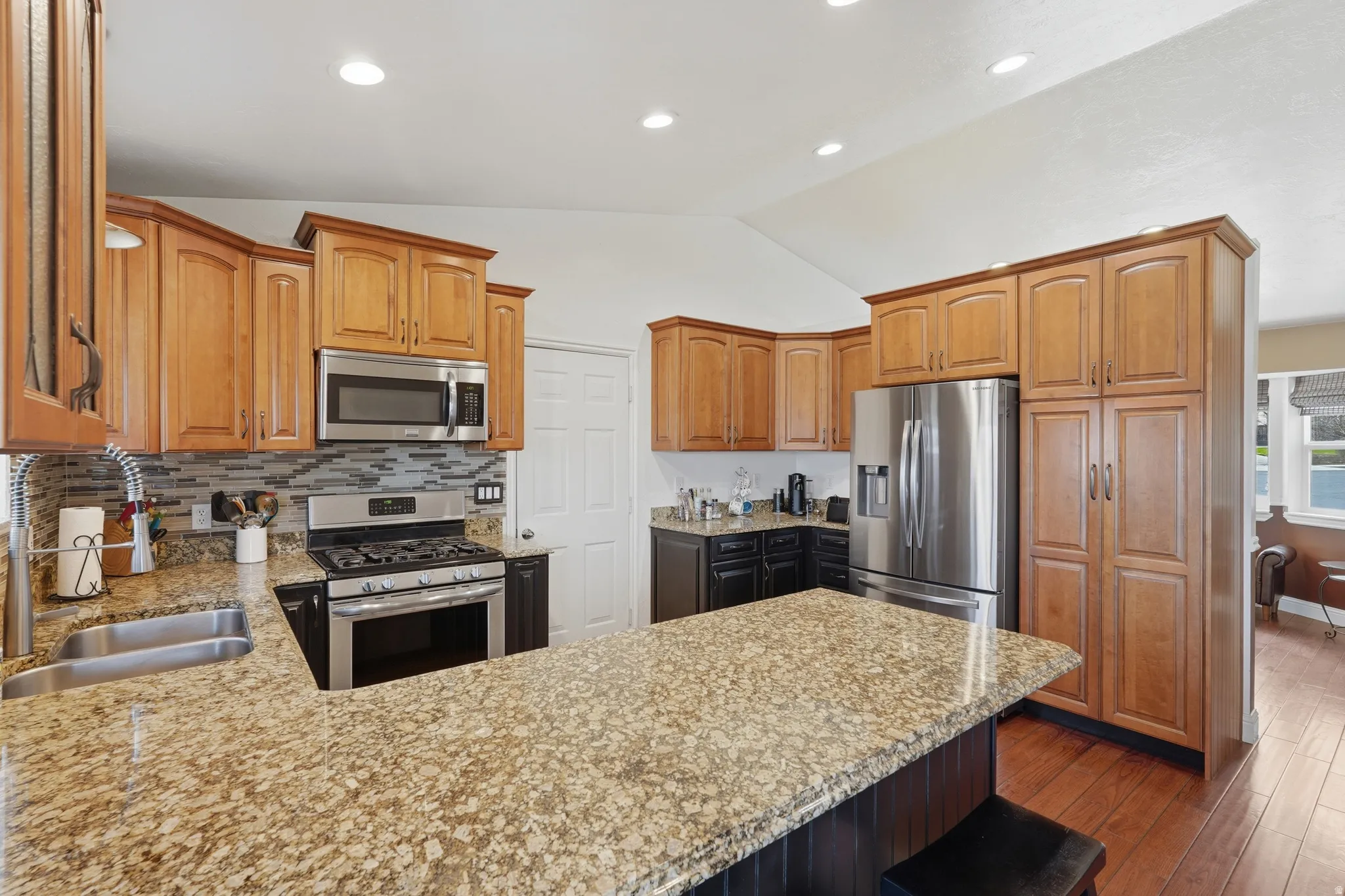 Kitchen featuring stainless steel appliances, vaulted ceiling, a peninsula, dark wood-type flooring, and wood finish cabinetry