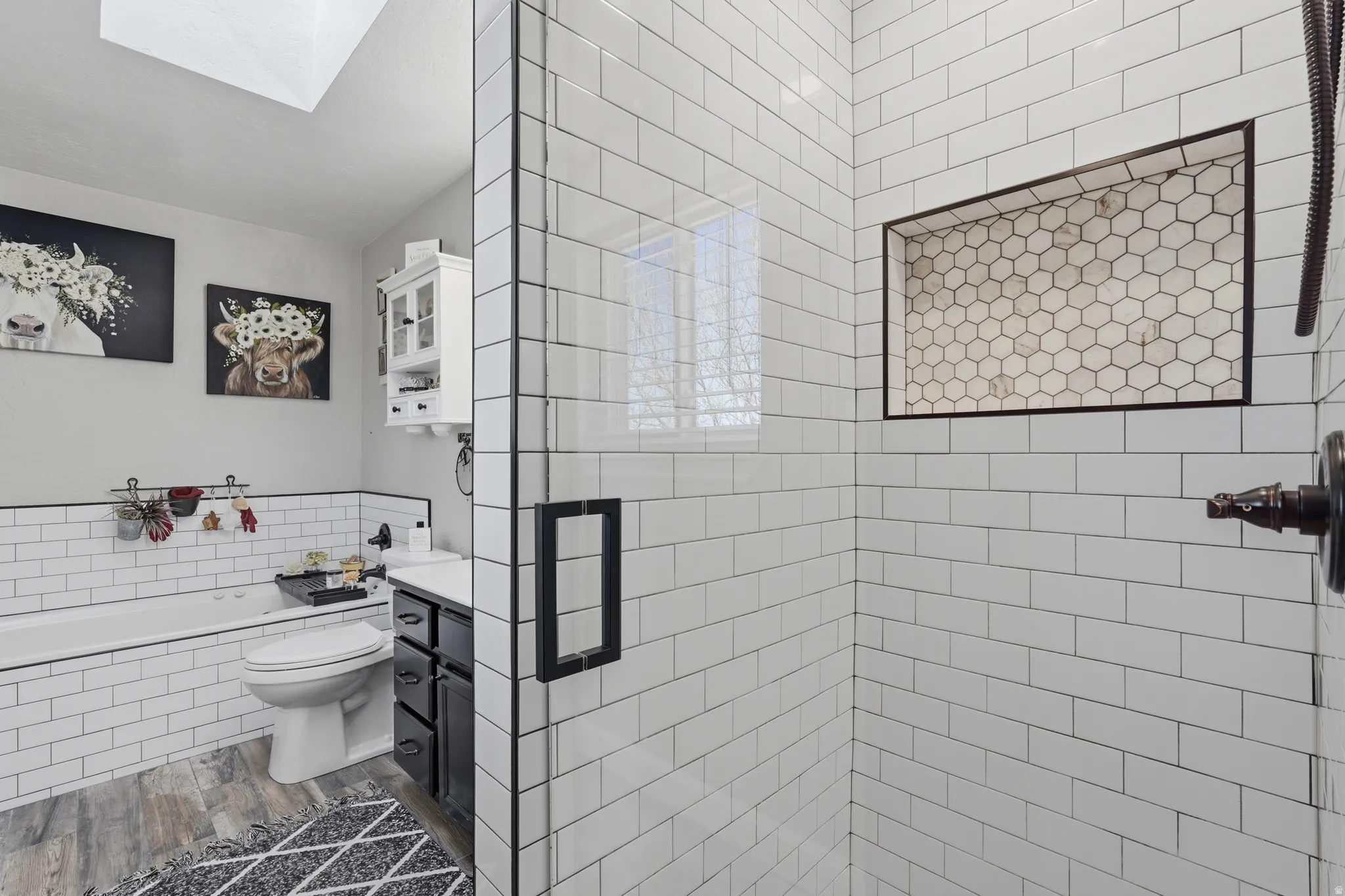 Full bath featuring vanity, a bath, a stall shower, a skylight, and dark wood-style flooring
