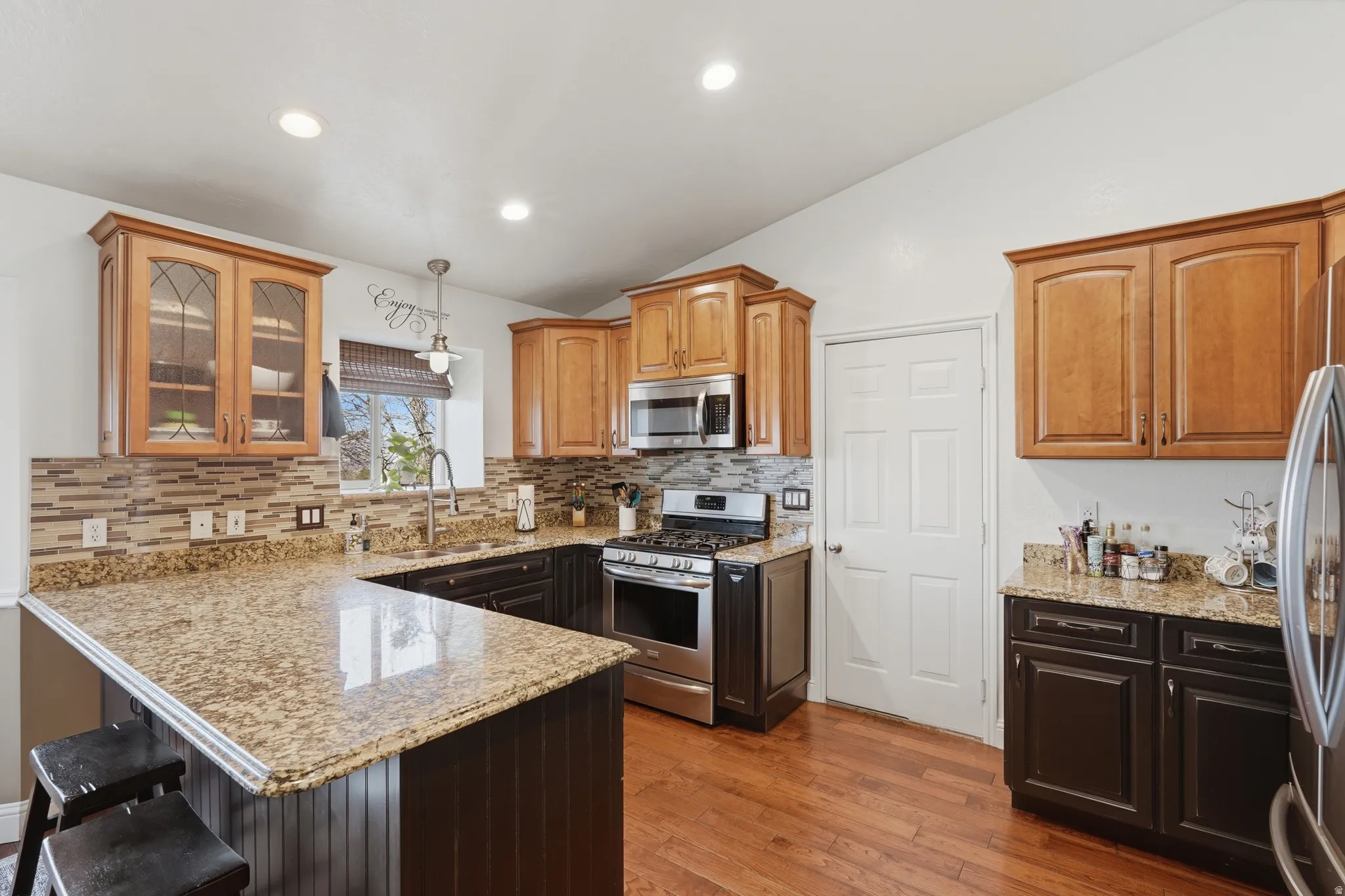 Kitchen featuring a kitchen breakfast bar, a peninsula, lofted ceiling, light stone counters, and stainless steel appliances