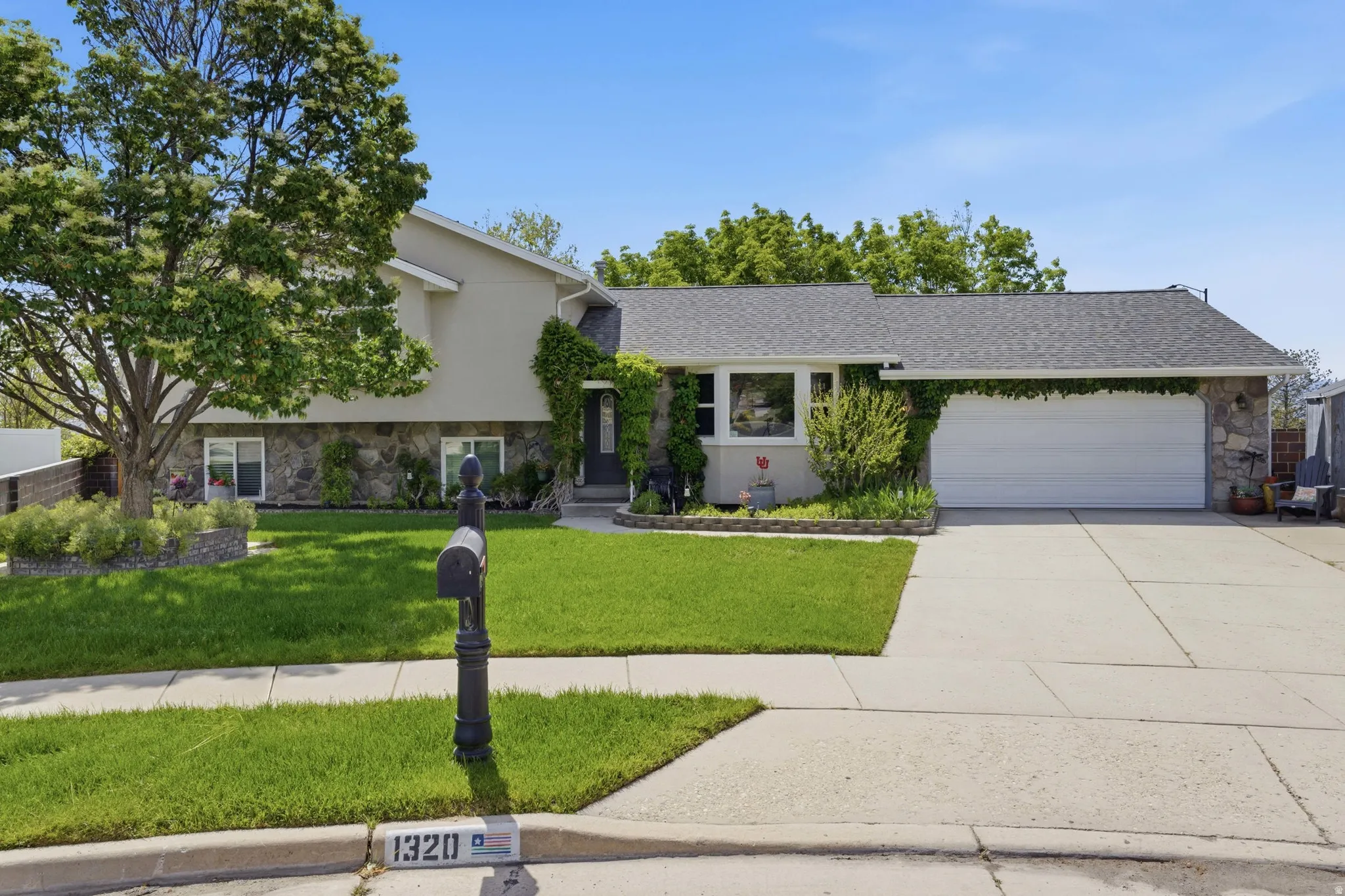 Two-story residence featuring a stone and stucco exterior, an attached two-car garage, and a manicured front lawn