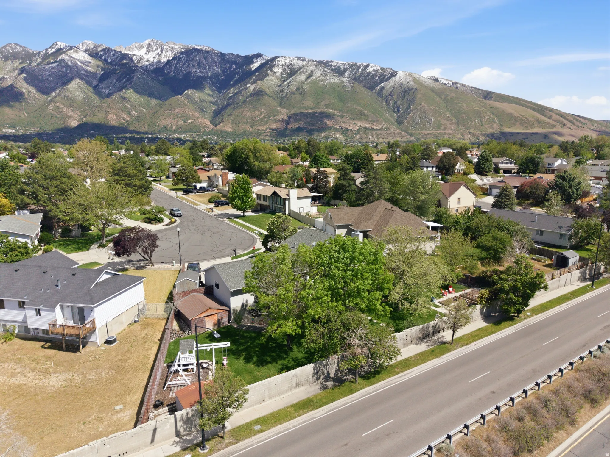 Expansive neighborhood setting featuring a paved road, mature trees, and mountainous terrain in the distance