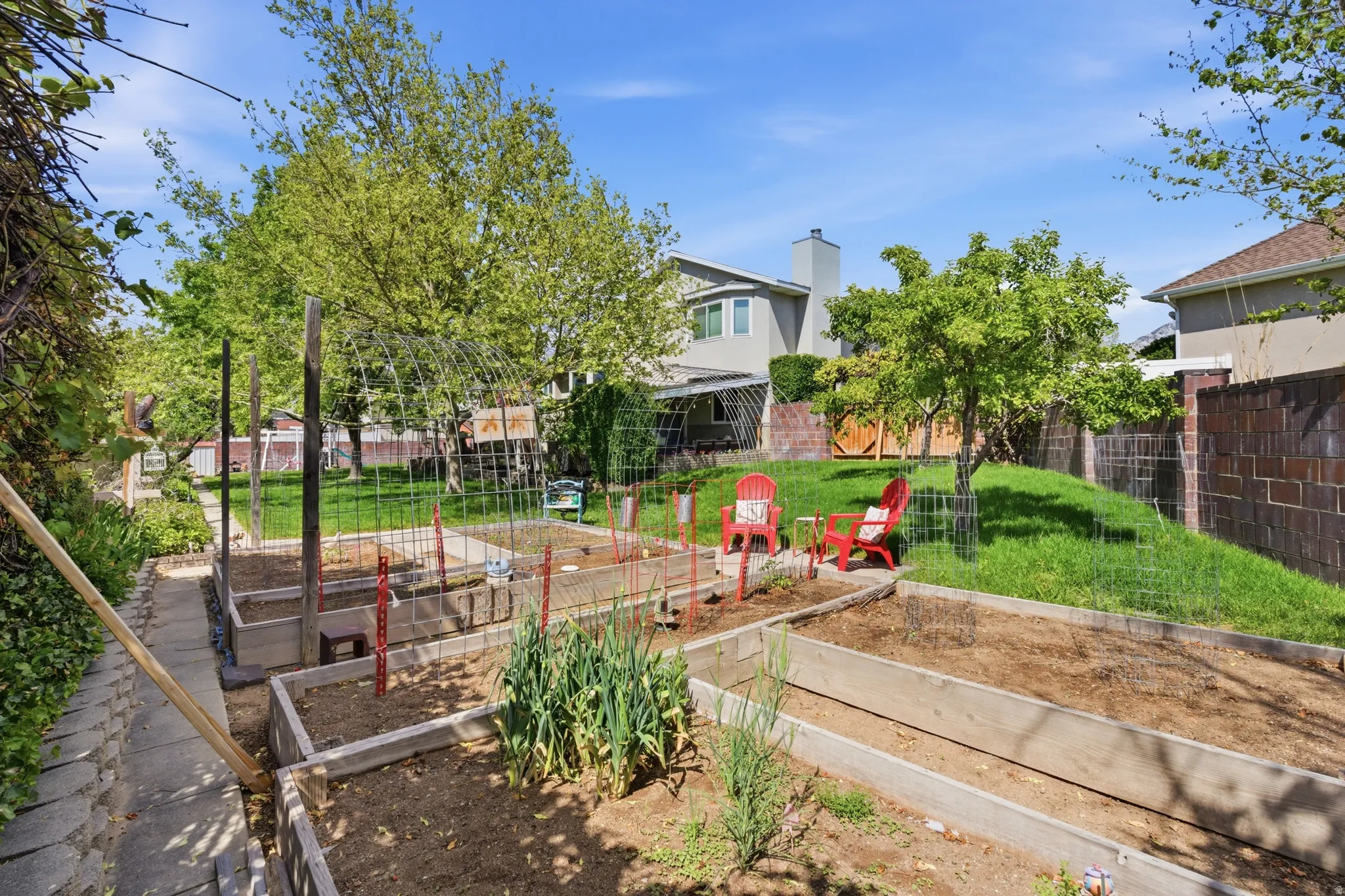 Tiered garden beds with established plantings, a paved pathway, and mature trees