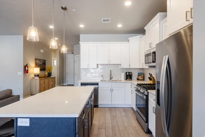 Two tone kitchen with stainless steel appliances, a center island, light stone countertops, open floor plan, and two tone cabinets