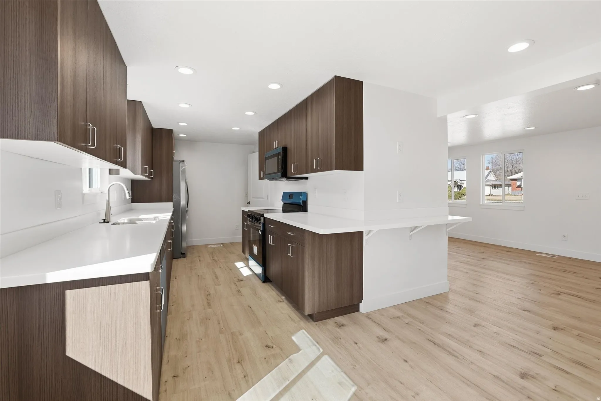 Kitchen featuring black range with electric cooktop, dark wood finish cabinetry, a kitchen bar, a peninsula, and light wood-style flooring