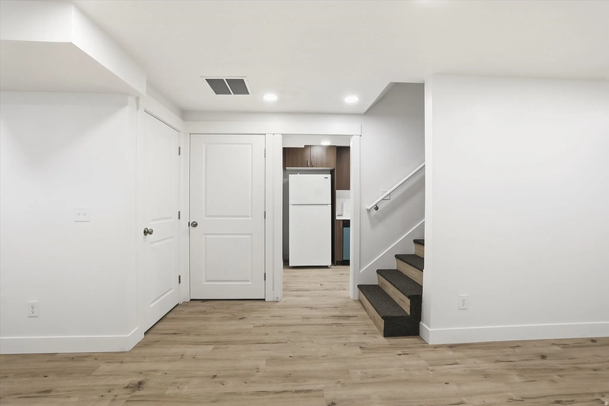 Finished basement with light wood finished floors, freestanding refrigerator, and recessed lighting